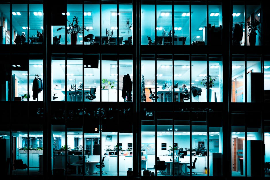 Night view of an illuminated modern office building showcasing workspaces through large windows